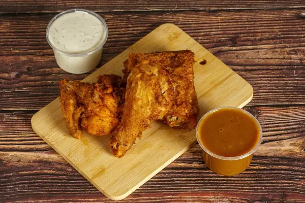 Two pieces of fried chicken on a board with a pot of curry sauce