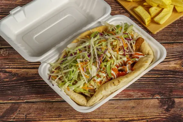 A kebab loaded with salad and sauce in a takeaway box